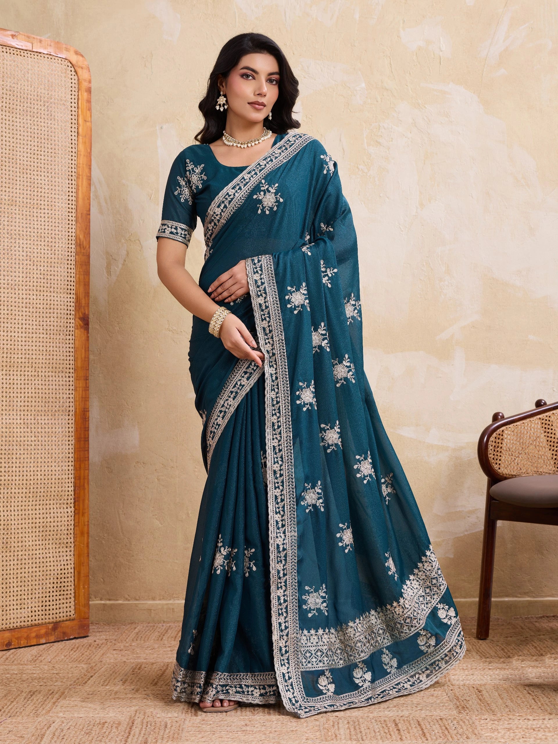 Woman wearing a teal saree with white patterns against a beige wall.